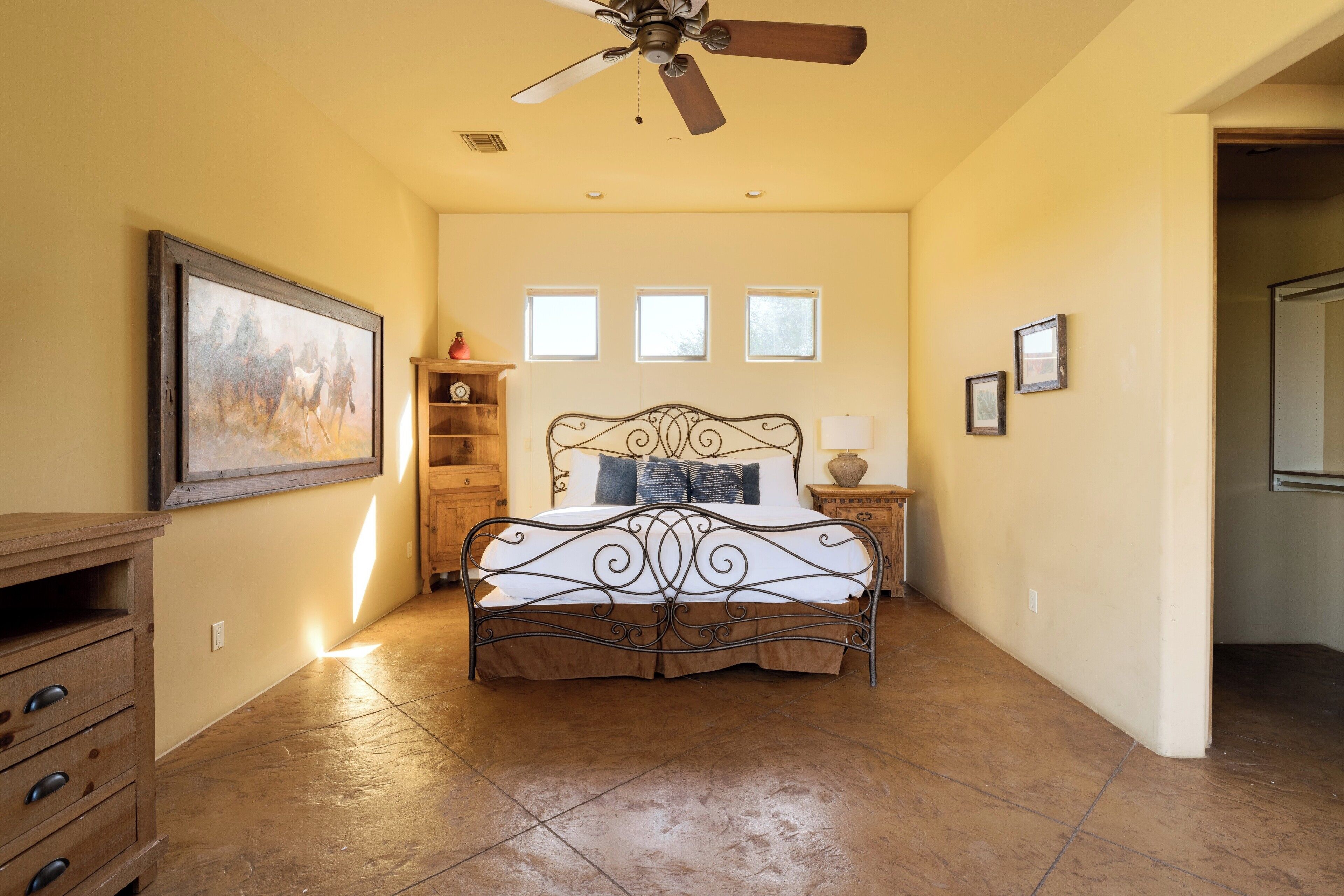 A bedroom with a bed, a ceiling fan, a wooden dresser, a framed picture, and a window.