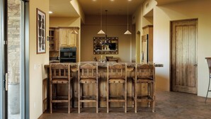 A kitchen with a central island, wooden bar stools, pendant lighting, and wooden cabinets.