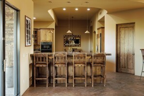 A kitchen with a central island, wooden bar stools, pendant lighting, and wooden cabinets.