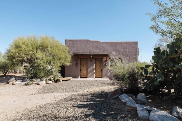 A building with two wooden doors, surrounded by desert vegetation and rocks. - Ocotillo Hills | Sleeps 16, 2 Casitas, 7BRs & Granite Mountain Hiking Trails (Scottsdale)