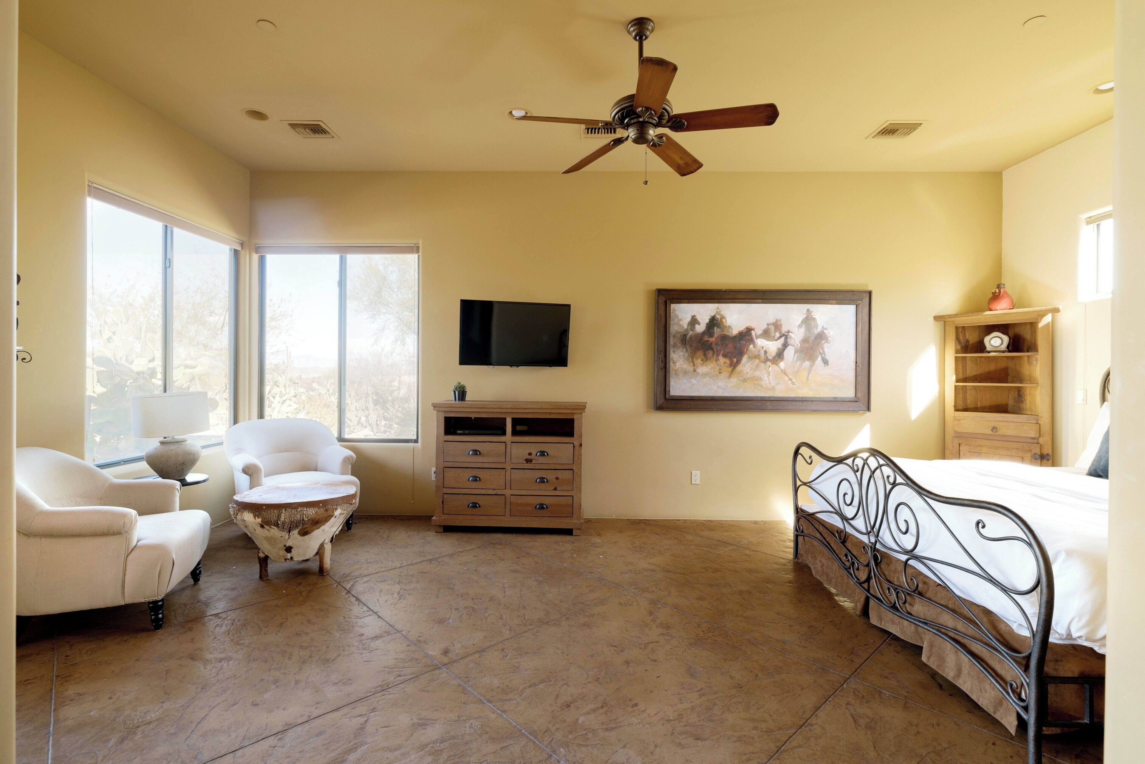 A spacious bedroom with a large bed, a ceiling fan, a TV, and a painting on the wall.