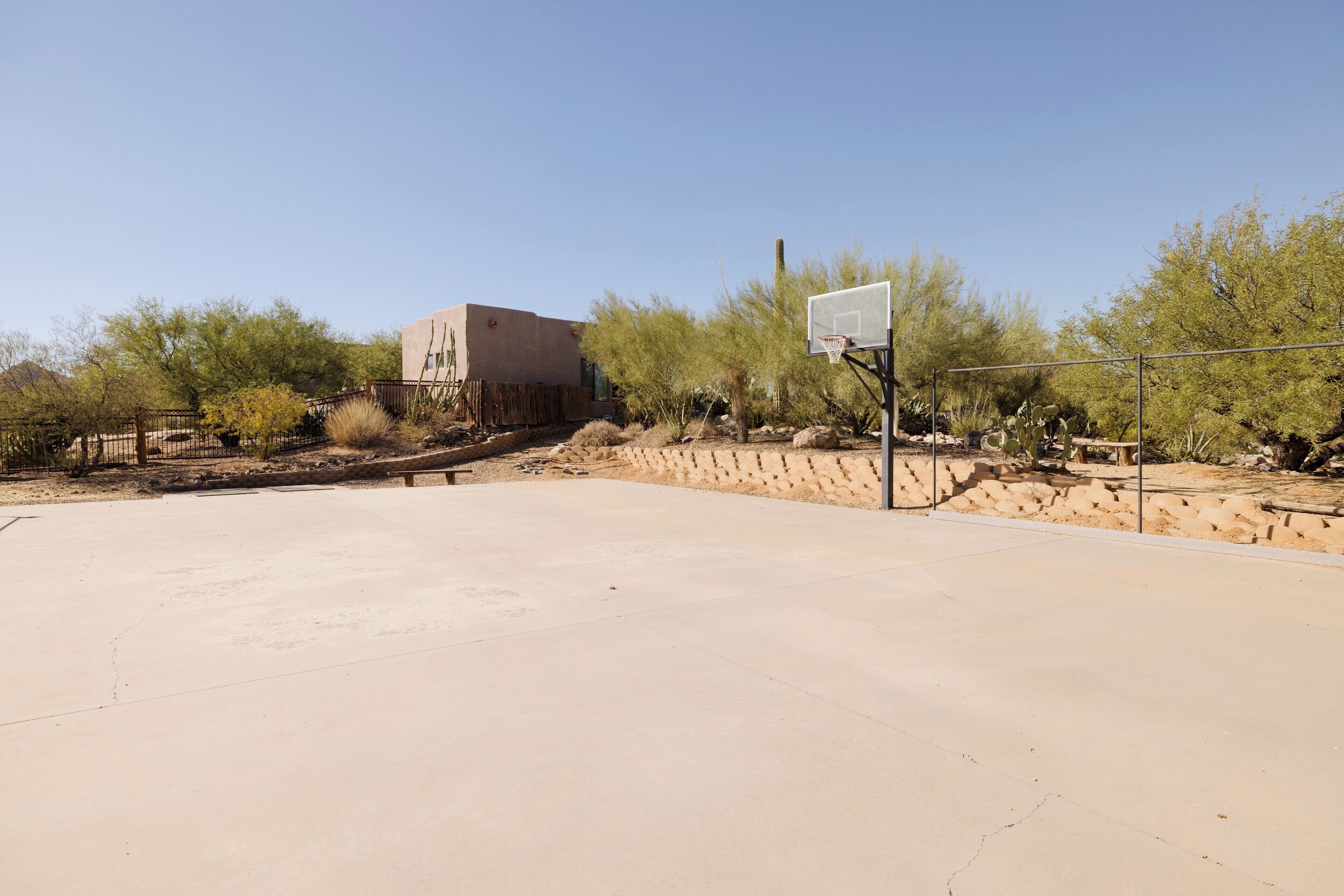 Una cancha de baloncesto al aire libre con valla de madera, aro de baloncesto y un edificio al fondo.