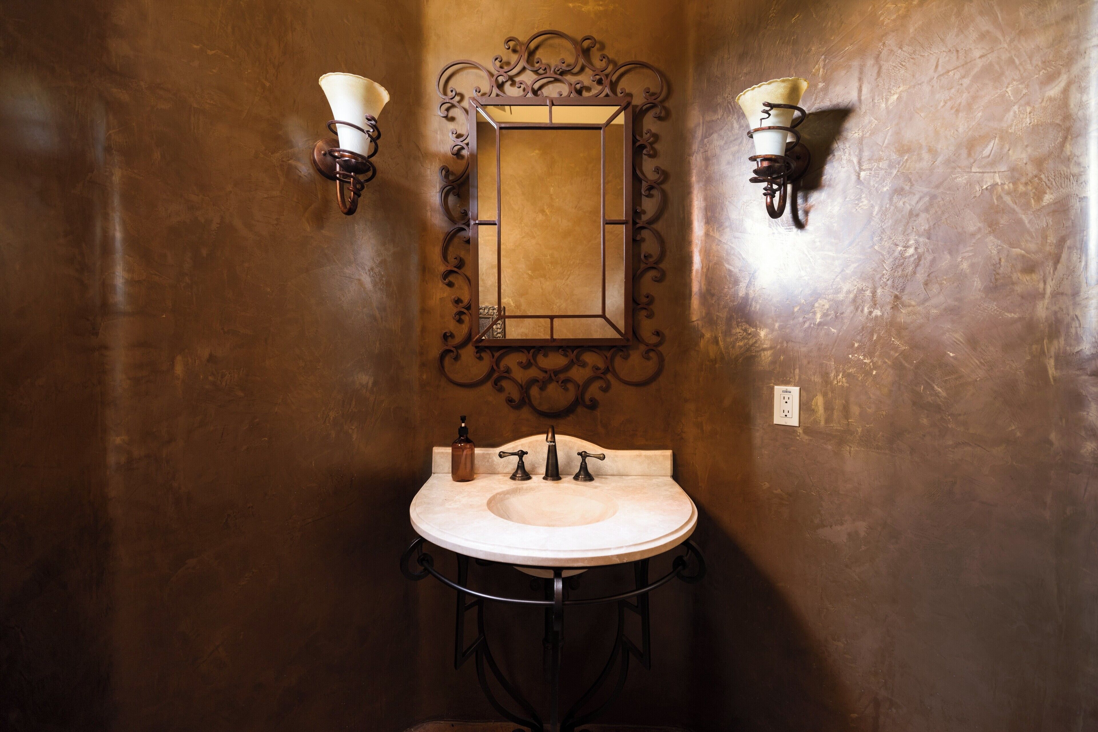 Un baño con un lavamanos redondo, dos luces empotradas en la pared y un espejo con un marco decorativo.