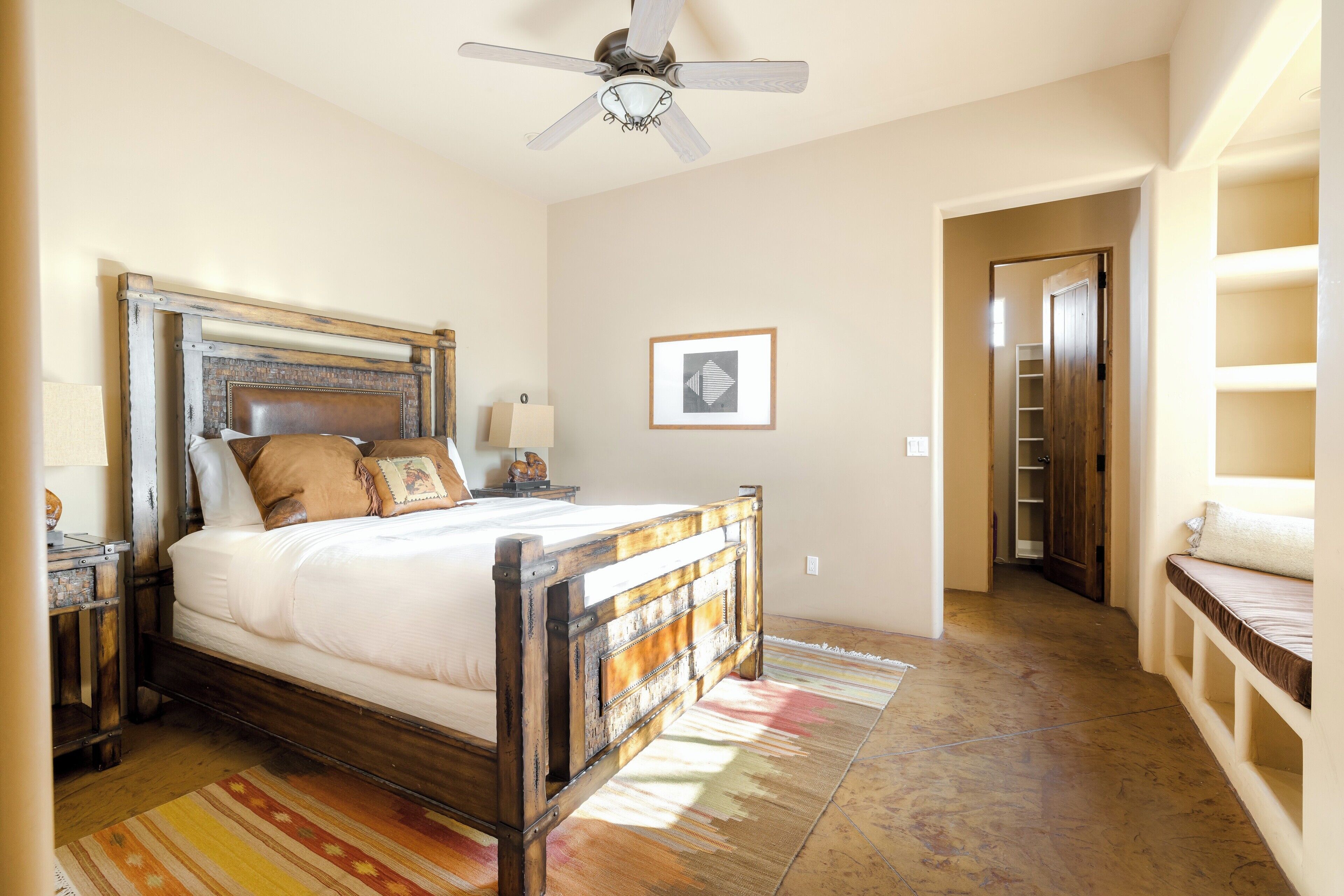 A bedroom with a wooden bed, a ceiling fan, a framed picture on the wall, and a walk-in closet.