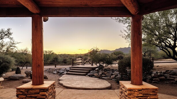 A covered patio with stone steps leading to a view of a sunset over a desert landscape.