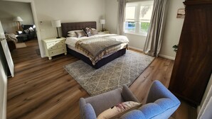 Ein Schlafzimmer mit Bett, Nachttischen, einem Schminktisch, einem Sessel, einem Deckenventilator und einem Fenster mit Vorhängen.