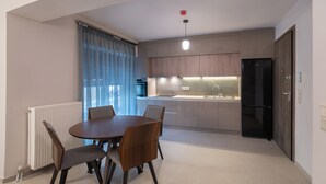 A modern kitchen with a dining area, featuring a round table and chairs, a built-in oven, and a refrigerator.