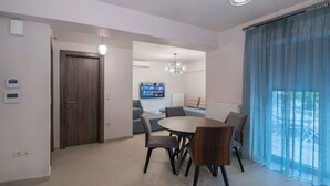 A modern living room with a dining area, a television, and a large window with curtains.