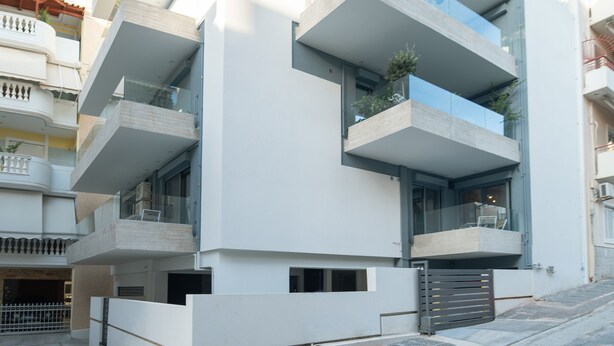 A modern multi-story building with balconies, large windows, and a gated entrance.