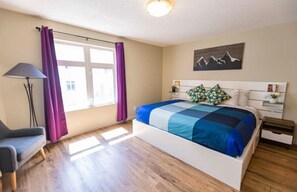 Relax in this serene bedroom with a large bed, bedside table, and a beautiful painting of mountains.