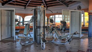 Ein Fitnessstudio mit verschiedenen Trainingsgeräten, großen Fenstern und einer hohen Decke mit freiliegenden Balken.