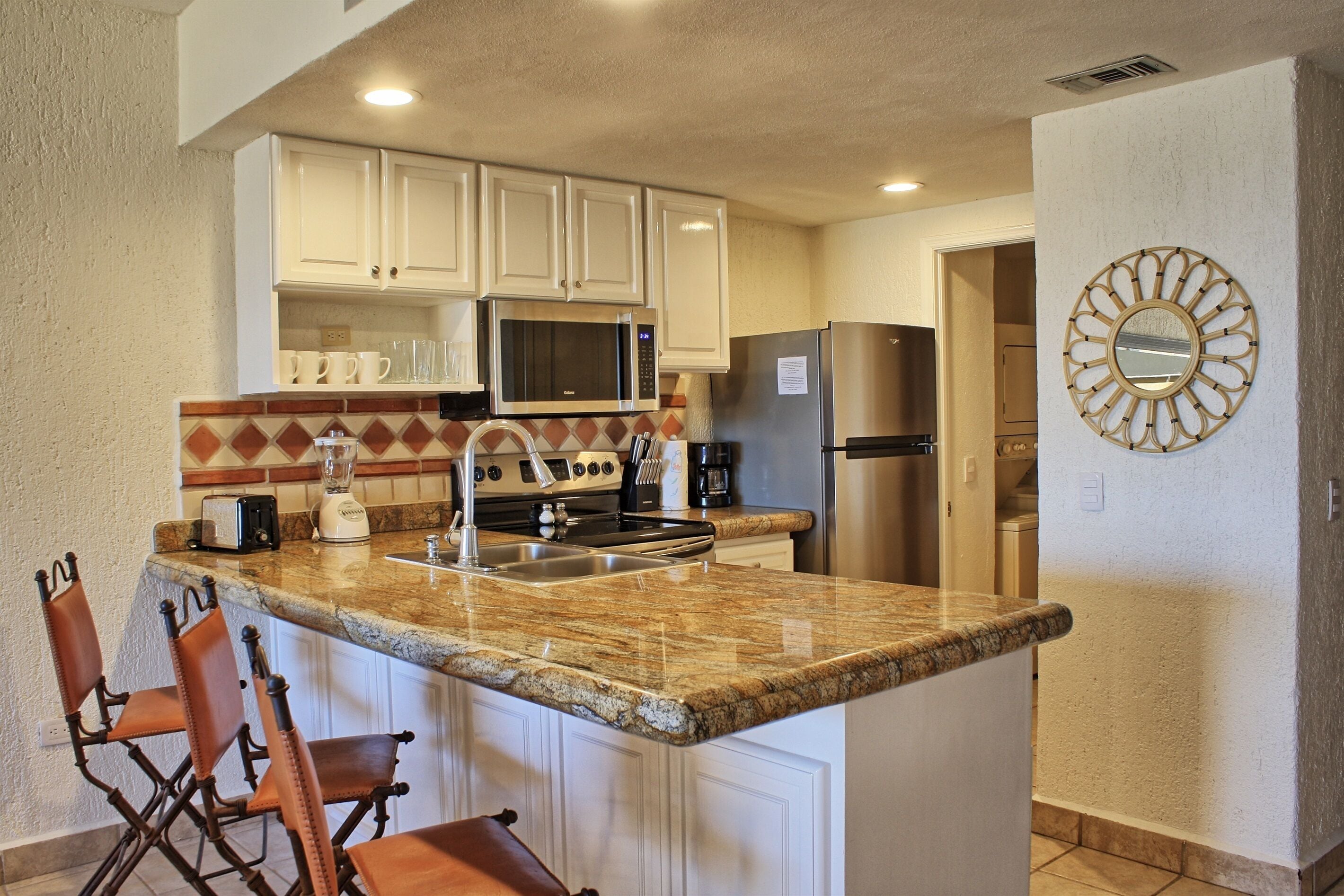 A kitchen with white cabinets, a granite countertop, a stainless steel refrigerator, and a microwave.