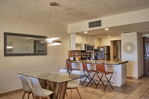 A modern kitchen with white cabinets, a central island, and a dining area with a glass table and chairs.
