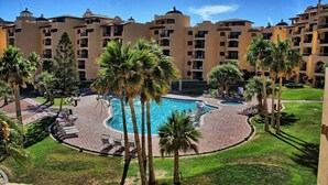 A hotel with a central swimming pool surrounded by palm trees and lounge chairs.