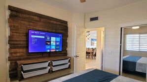 A bedroom with a large bed, a mounted TV displaying a streaming service interface, and a wooden accent wall.