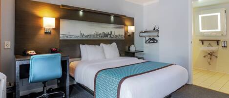 Una habitación de hotel con cama, escritorio, silla y un cuadro de paisaje urbano en la pared.