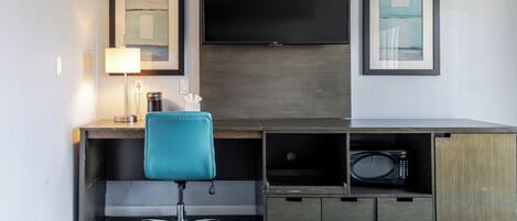 Habitación de hotel con escritorio, una silla, televisor y microondas.