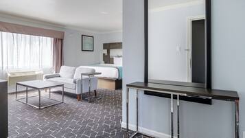 A hotel room with a bed, a desk, a chair, a large mirror, and a window with curtains.