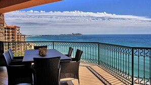 A balcony with a table and chairs, overlooking a coastal view with a clear sky and a distant island.