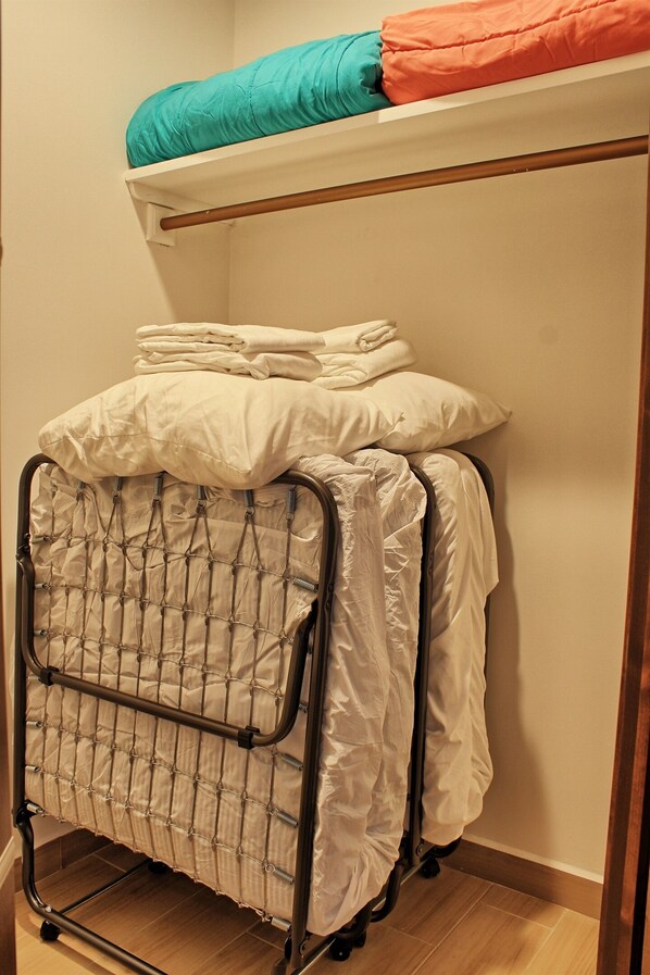 Un lit superposé avec un matelas sur le lit du haut et une étagère en métal avec des couvertures et des oreillers pliés en dessous.