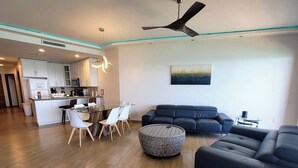 A modern living room with a dining area, a kitchen in the background, and a ceiling fan.