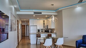 A modern kitchen with white cabinets, a glass dining table, and a blue accent wall.