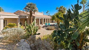 A building with a pool, surrounded by cacti and palm trees.