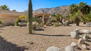 A desert landscape with a building featuring a patio area surrounded by cacti and rocks.