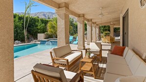 A covered outdoor seating area with a pool, lounge chairs, and a view of mountains.