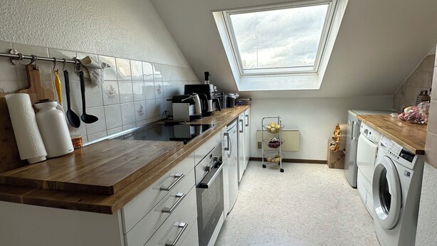 Una cocina moderna con tragaluz, armarios blancos y encimera de madera.