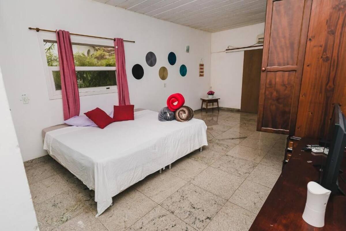 A room with a bed, a window with curtains, a small table, and a wooden door.
