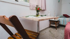 Et hyggeligt, lille værelse med en træstol, et bord med en vase blomster, en seng med et farverigt tæppe og et vindue med gardin.
