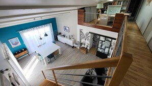 A spacious loft apartment with a dining area, kitchen, and a staircase leading to an upper level. - Villa proche de La Rochelle avec piscine (VILLEDOUX)