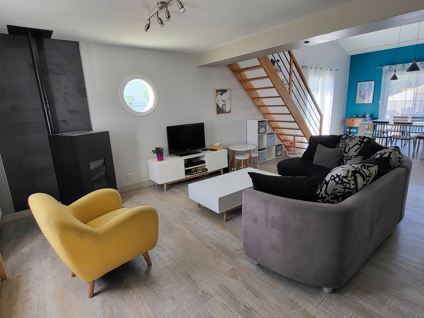 A modern living room with a sofa, a yellow armchair, a TV, and a staircase leading to a balcony.