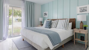 A bedroom with a large bed, a nightstand, a lamp, and a window with curtains. - Iconic Mid-Century Modern Gem – Featured on Palm Springs Modernism Week Tour! (Palm Springs)