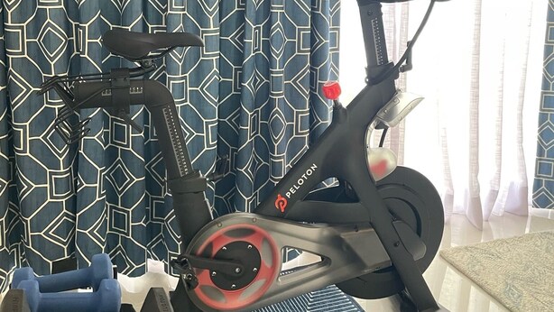 A stationary bike with a heart-shaped display, a pair of dumbbells, and a patterned exercise mat in a room with patterned curtains. - Iconic Mid-Century Modern Gem – Featured on Palm Springs Modernism Week Tour! (Palm Springs)