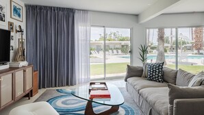 A modern living room with a glass coffee table, a sofa, and a view of a pool and outdoor area. - Iconic Mid-Century Modern Gem – Featured on Palm Springs Modernism Week Tour! (Palm Springs)