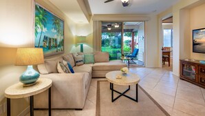 Ein Wohnzimmer mit einem beigen Sofa, einem runden Couchtisch, einem Deckenventilator und einem Gemälde mit Strandmotiv.