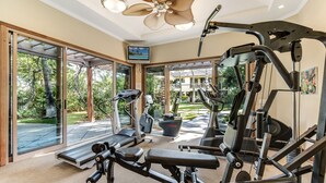 Ein Heimfitnessraum mit Trainingsgeräten, großen Fenstern und einem Deckenventilator.