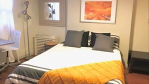 A neatly made bed with a striped bedspread and an orange blanket, a bedside table with a lamp, a chair, and a framed picture on the wall. - SPIFFY PRIVATE APT. WILLIAMSBURG PRIME BROOKLYN (Brooklyn)
