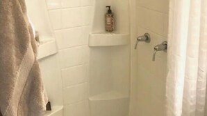 A small, white-tiled shower area with a showerhead, a soap dispenser, and a shelf. - SPIFFY PRIVATE APT. WILLIAMSBURG PRIME BROOKLYN (Brooklyn)