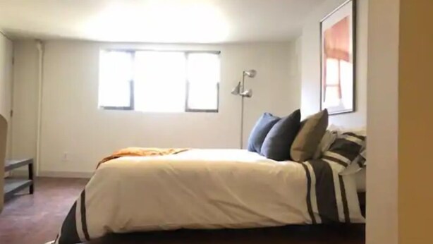 A bedroom with a bed, a window, and a wall-mounted lamp. - SPIFFY PRIVATE APT. WILLIAMSBURG PRIME BROOKLYN (Brooklyn)