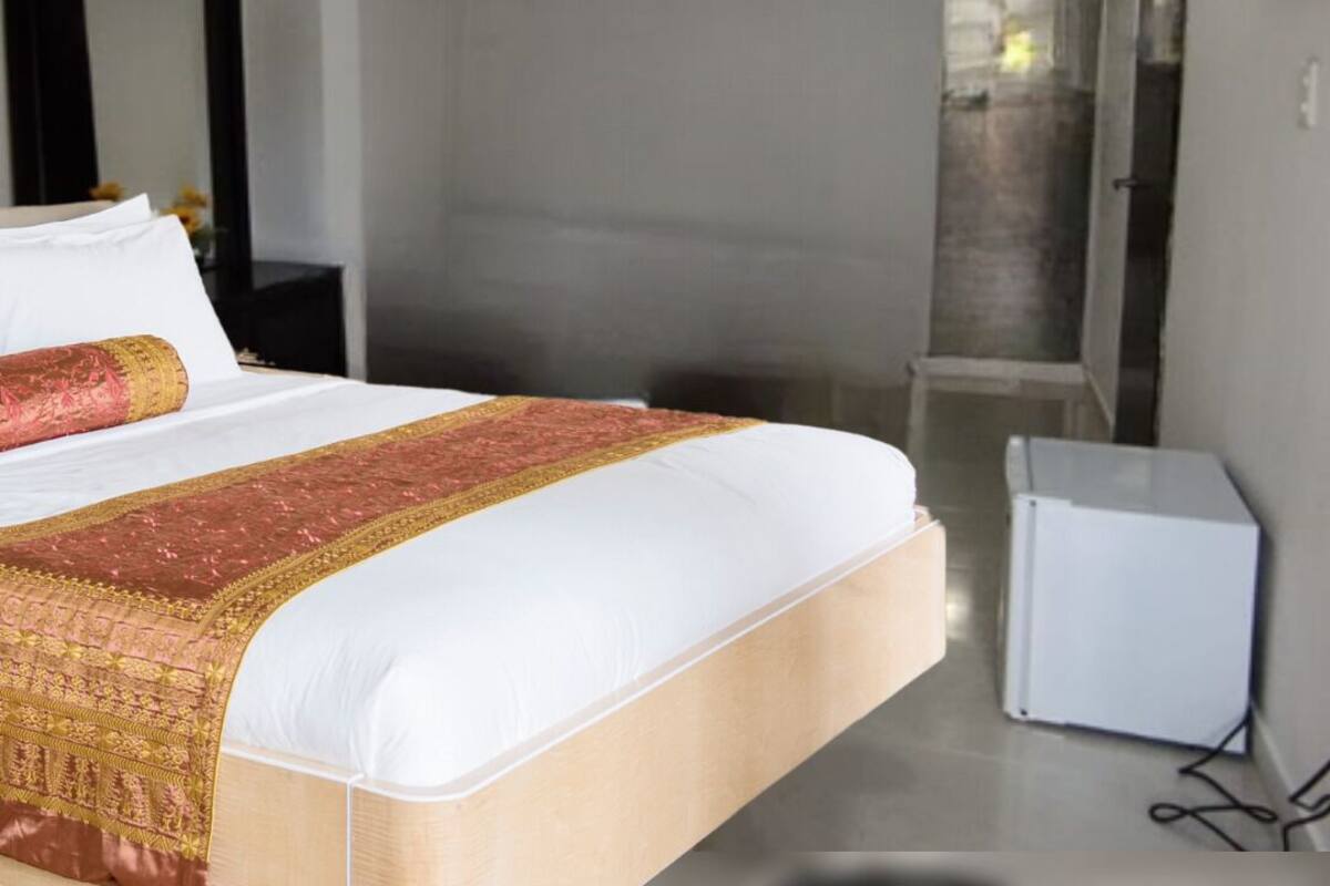 Habitación de hotel con una cama grande, una mesita de noche, un armario pequeño blanco y un televisor fijado a la pared.