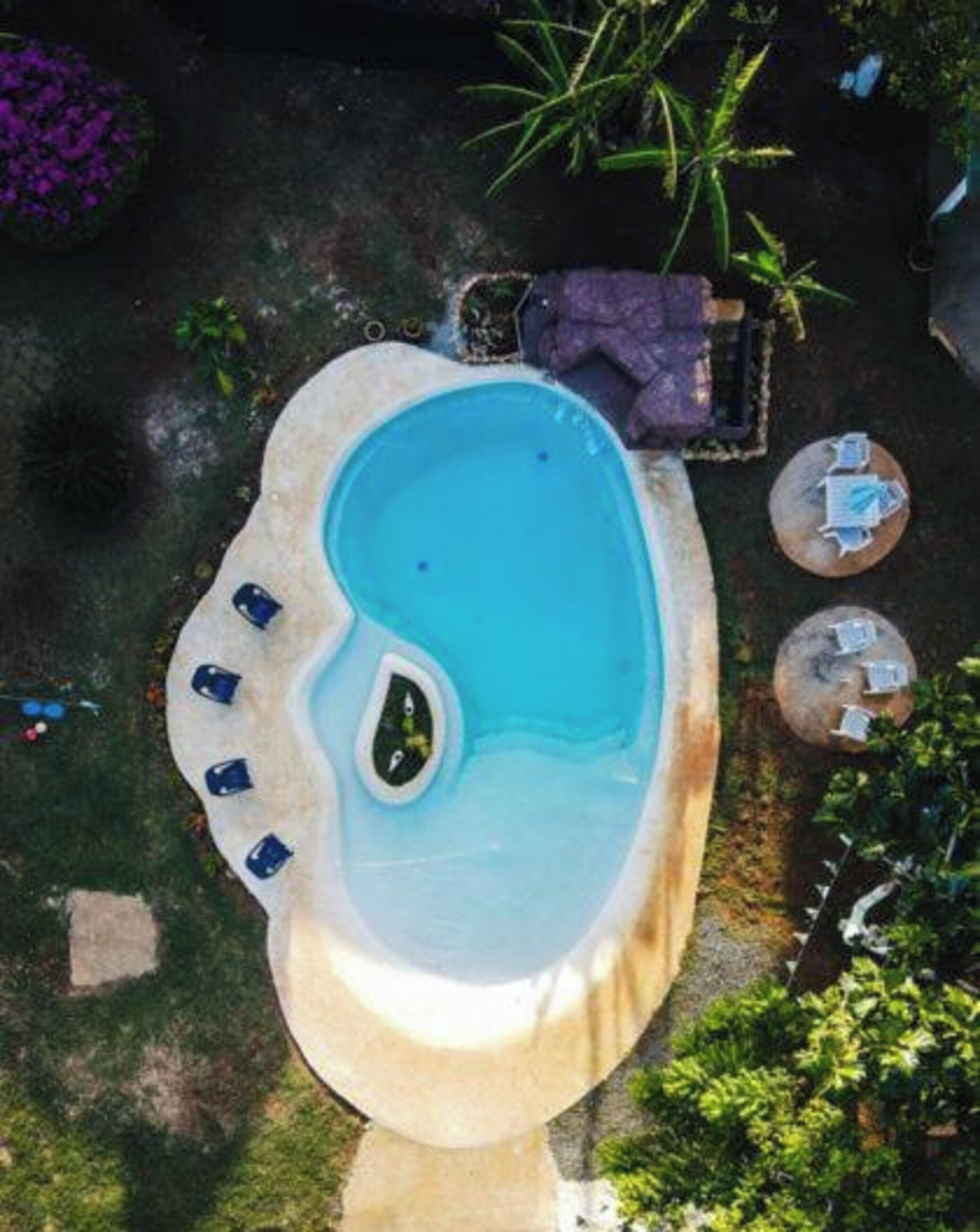 A small, irregularly shaped swimming pool with a few lounge chairs and a hot tub.