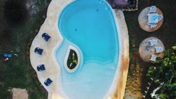 A small, irregularly shaped swimming pool with a few lounge chairs and a hot tub.