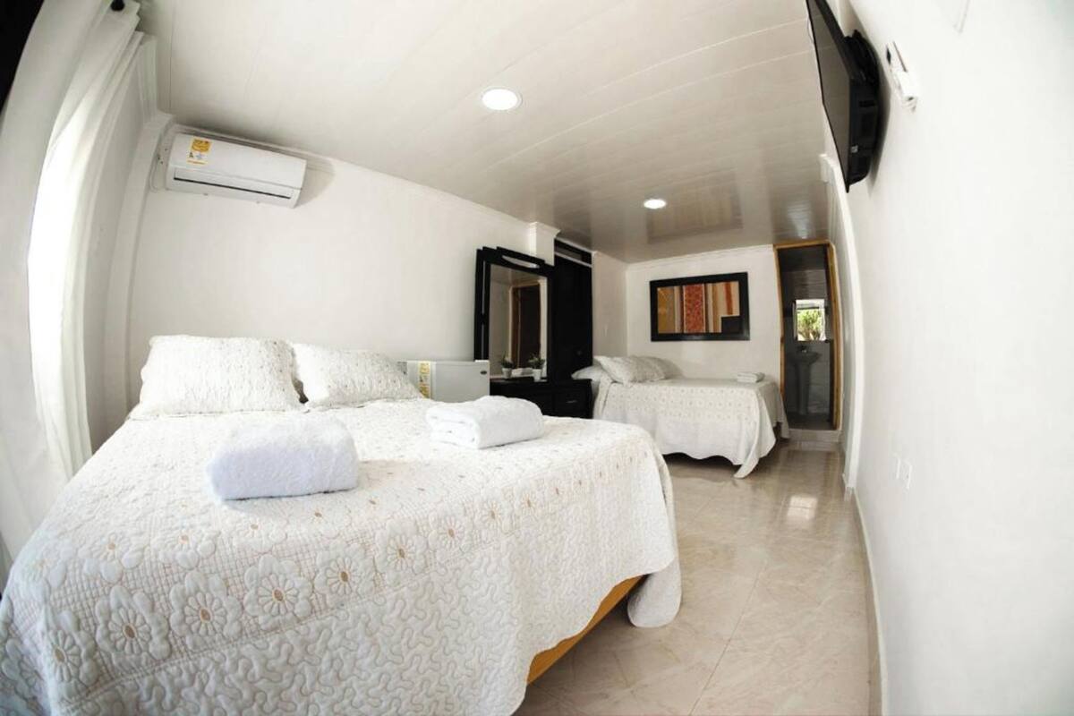 Una habitación de hotel con dos camas, un aire acondicionado, una televisión y una mesita.