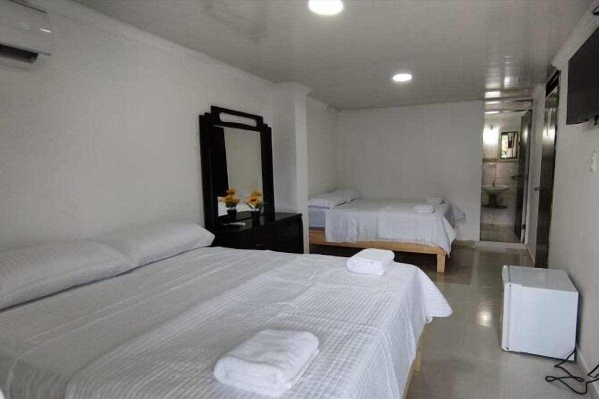 Una habitación de hotel con dos camas, un espejo, un televisor y un mueble blanco pequeño.