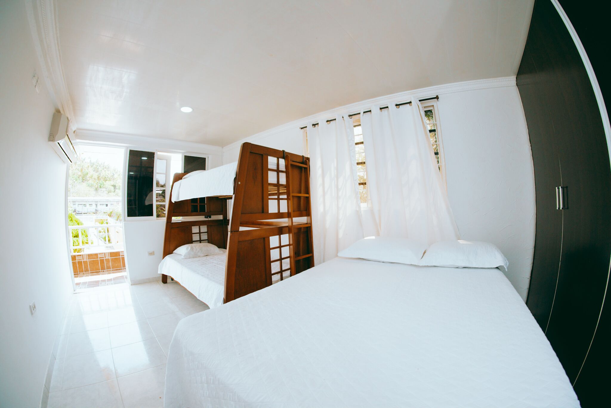 Un dormitorio con una cama nido, una cama individual, una silla de madera y un armario.