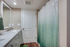 Une salle de bain avec une porte blanche, un lavabo avec un miroir et une douche avec un rideau vert.