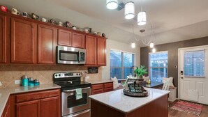 A kitchen with wooden cabinets, stainless steel appliances, and a central island. - Patio, Pergola & Pool Access: Aubrey Retreat! (Aubrey)